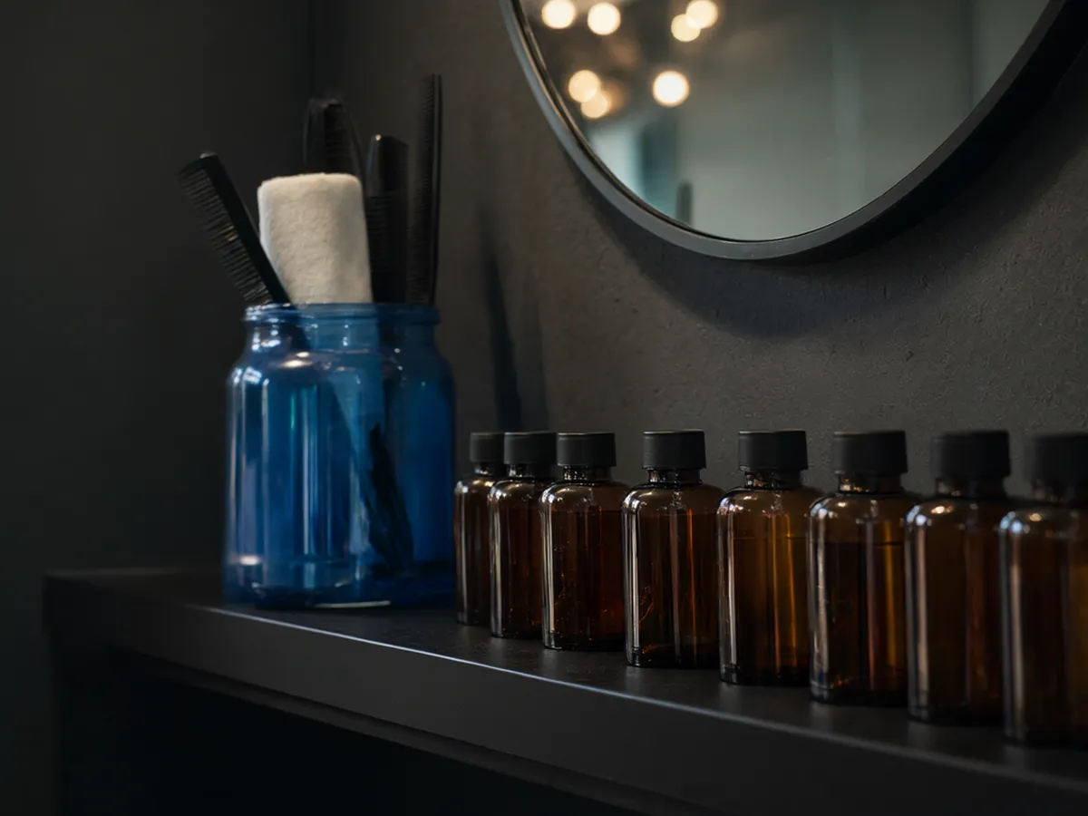 A barber station with a round mirror, amber tonic bottles and a jar of combs