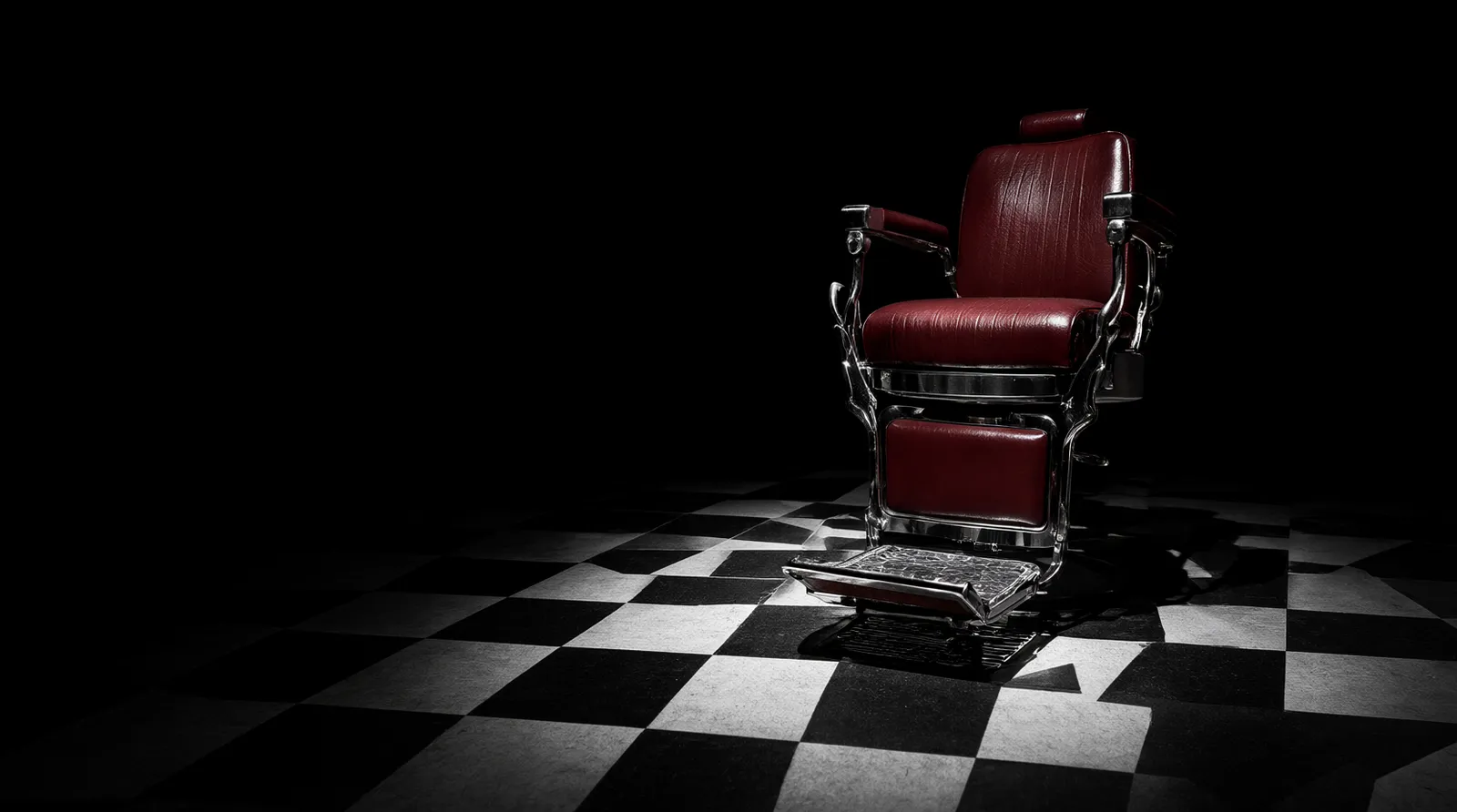 A red leather barber chair under a spotlight on a black and white checkered floor